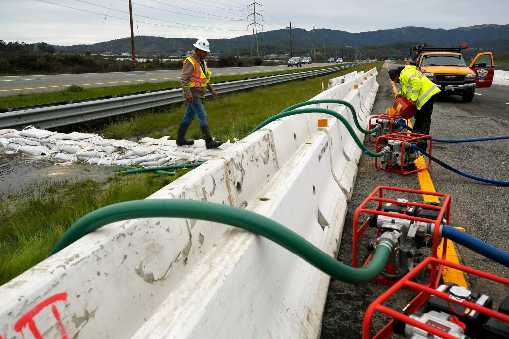 Jose Lopez Guzman, left, and Victor Castillo of Ghilotti Brothers construction company check hoses and refuel pumps directing flood water out of the median of Highway 37, where water levels rose after a levee break on Novato Creek, flooding the highway near Novato, California, on Friday, March 1, 2019. (Alvin Jornada / The Press Democrat)