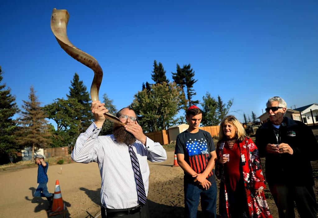 Rabbi Mendel Wolvovsky of Chabad Jewish Center uses a shofar to help bless the rebuilding of a home razed in the Tubbs fire belonging to Barbara Winestock, middle and her son Dylan Chadwick, 19, in Coffey Park, Monday, August 27 in Santa Rosa. At right is congregation member Joseph Wand. (Kent Porter / The Press Democrat) 2018