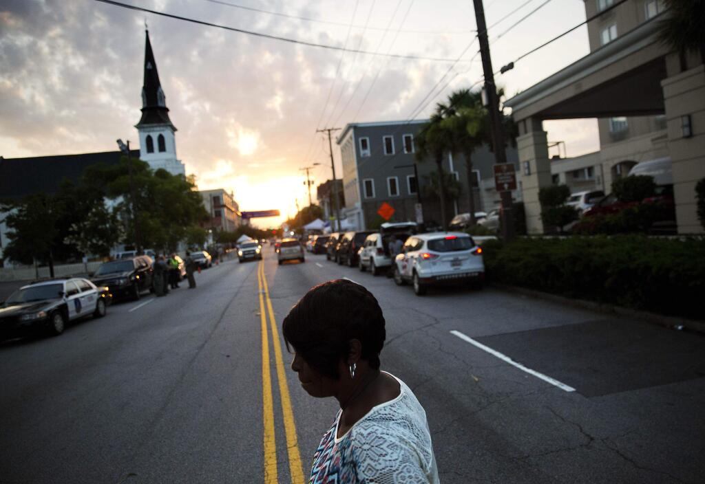 A woman crosses the street on her way to visit a sidewalk memorial to the Emanuel African Methodist Episcopal Church shooting victims as the sun rises next to the church's steeple Sunday, June 21, 2015, in Charleston, S.C. Congregation members say the historic black church where nine people were killed is going to re-open for Sunday morning service. (AP Photo/David Goldman)