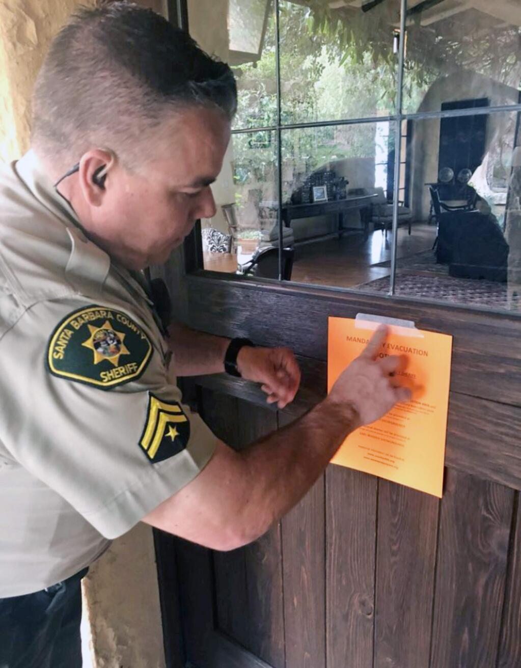 Santa Barbara County Sheriff's Deputy Mike Harris posts a notice on a home near Carpinteria, Calif., advising of the mandatory evacuation notice due to forecast rain and possible debris flow due to the recent Thomas Fire Thursday, March 1, 2018. A major winter storm swept south through California on Thursday, bringing heavy snow and strong winds to mountains and steady rain elsewhere, while prompting mandatory evacuations for coastal areas to the south that were devastated by deadly mudslides in January. As many as 30,000 people were ordered to leave an area of Santa Barbara County before the storm arrived early Friday. (Mike Eliason/Santa Barbara County Fire Department via AP)