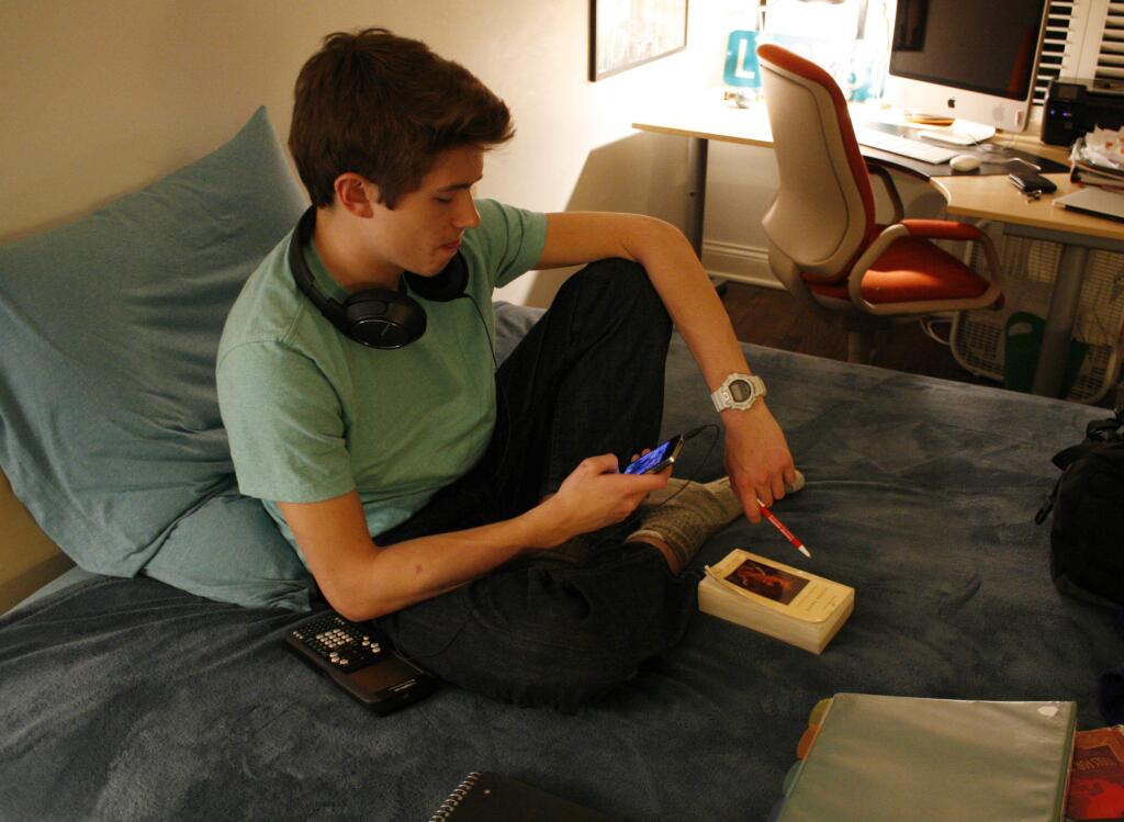 Donald Conkey, 15, checks his smartphone while doing homework in Wilmette, Ill. The World Health Organization says that teens need more vigorous physical activity. (MARTHA IRVINE / Associated Press)