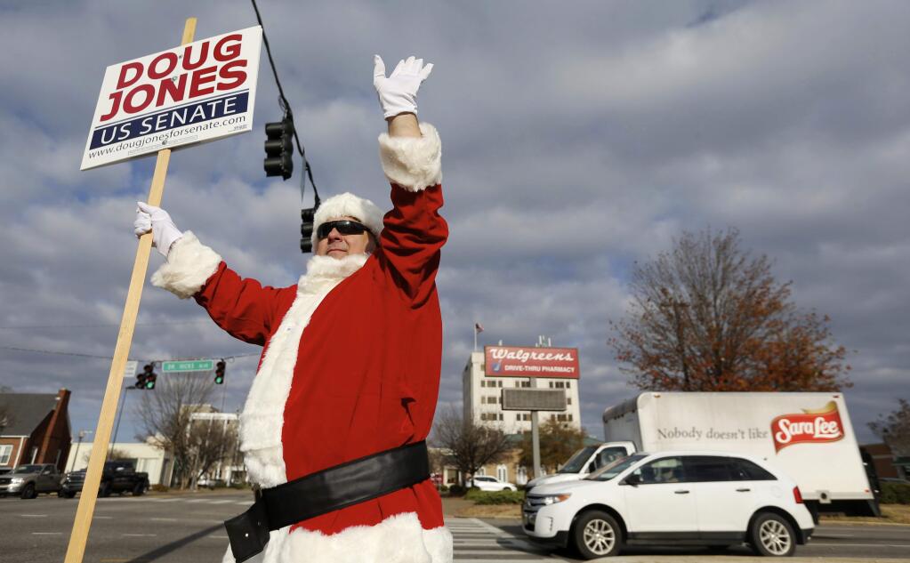 David Watson waves in a Santa suit as he holds a Doug Jones sign Tuesday, Dec. 12, 2017 in Florence, Ala. Watson, who just got off a 12 hour work shift, is moving around to different intersections in the Shoals to hold the sign for the candidate he wants to win the special U.S. Senate election. (Allison Carter/The TimesDaily via AP)