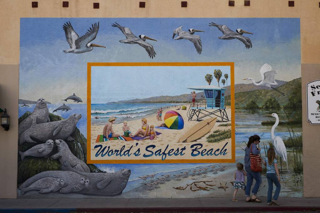 In this Thursday, April 12, 2018, photo, visitors walk past a mural on their way to a farmers' market in Carpinteria, Calif. Carpinteria, about 85 miles (137 kilometers) northwest of Los Angeles, is located on the bottom of Santa Barbara County, a tourist area famous for its beaches, wine and temperate climate. It's also gaining notoriety as a haven for cannabis growers. (AP Photo/Jae C. Hong)