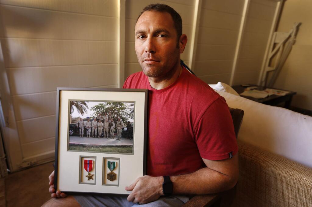 Robert D'Andrea, a retired Army major and Iraq war veteran, holds a frame with a photo of his team on his first deployment to Iraq on Friday, Oct. 21, 2016 in his home in Los Angeles. Nearly 10,000 California National Guard soldiers have been ordered to repay huge enlistment bonuses a decade after signing up to serve in Iraq and Afghanistan. The Pentagon demanded the money back after audits revealed overpayments by the California Guard under pressure to fill ranks and hit enlistment goals. If soldiers refuse, they could face interest charges, wage garnishments and tax liens, D'Andrea said he was told to repay his $20,000 because auditors could not find a copy of the contract he says he signed. (Al Seib/Los Angeles Times via AP)