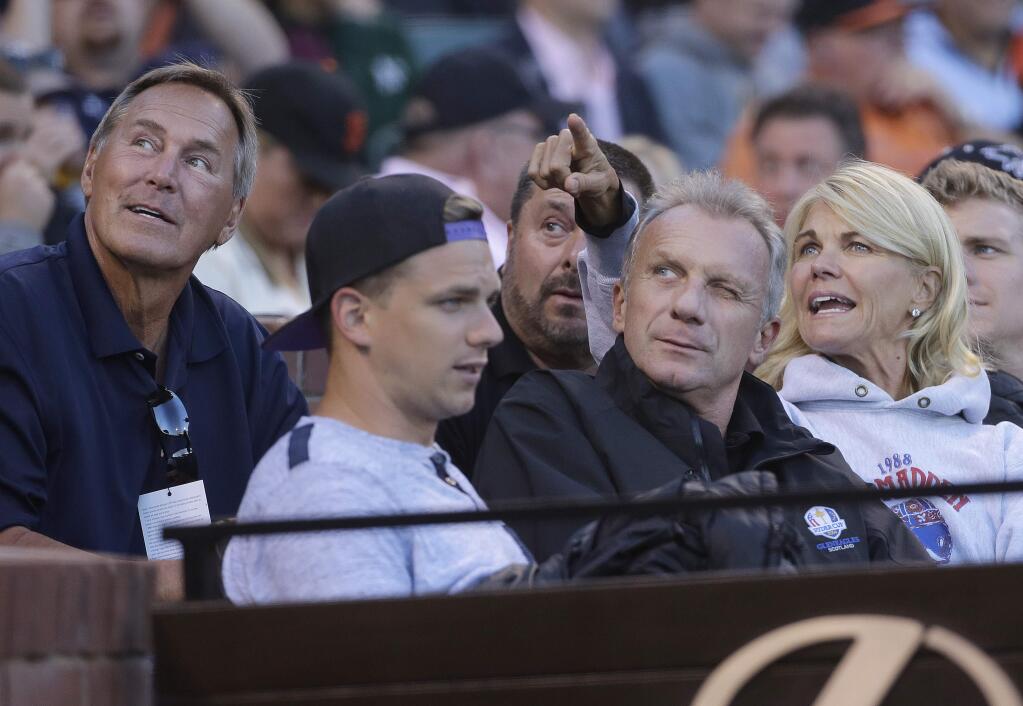 Former football player Dwight Clark, left, looks up with Joe Montana, center left, and Montana's wife Jennifer during the third inning of an interleague baseball game between the San Francisco Giants and the Oakland Athletics in San Francisco, Monday, June 27, 2016. (AP Photo/Jeff Chiu)
