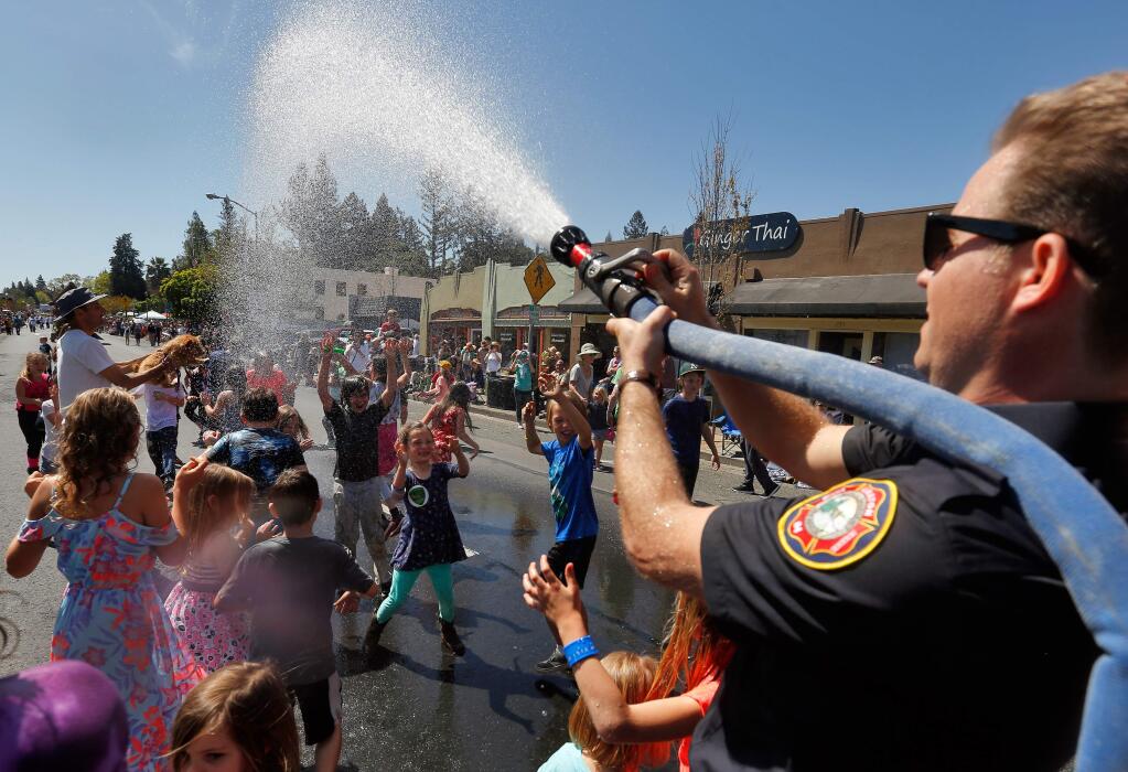 Graton Fire Protection District firefighter trainee Matt Skinner sprays water over a crowd of children and other spectators as the Apple Blossom Parade progresses along South Main Street in Sebastopol, California, on Saturday, April 21, 2018. (Alvin Jornada / The Press Democrat)