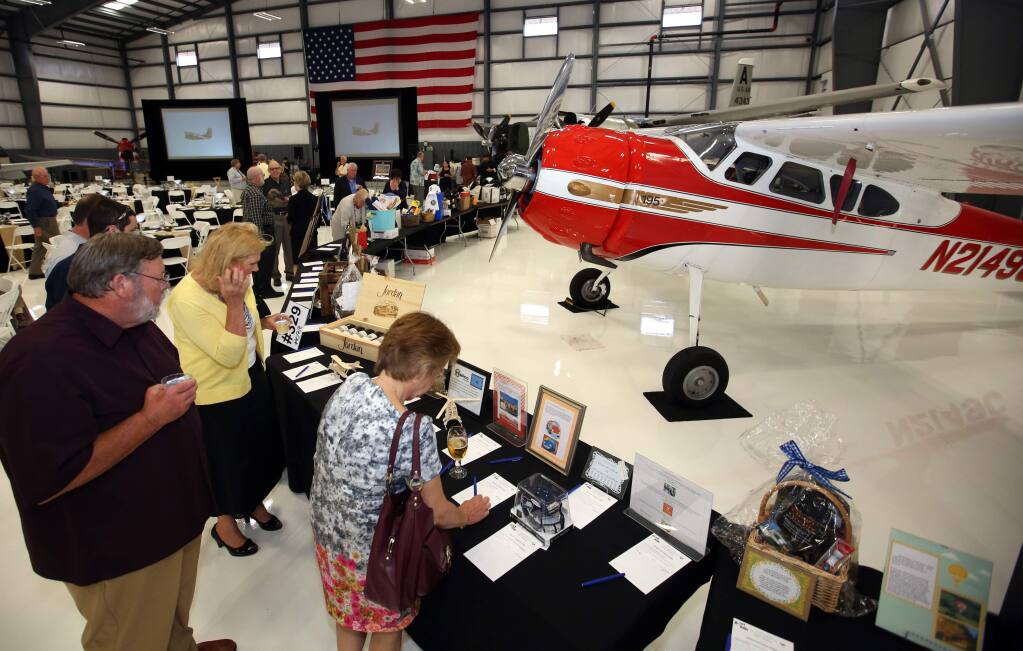 Guests check out the silent auction items during the Mustang Round-Up dinner, program and raffle to kick off the Pacific Coast Air Museum's annual Wings Over Wine Country air show held at the Vine Jet Hangar, Friday, Sept. 19, 2014. (Crista Jeremiason/The Press Democrat)