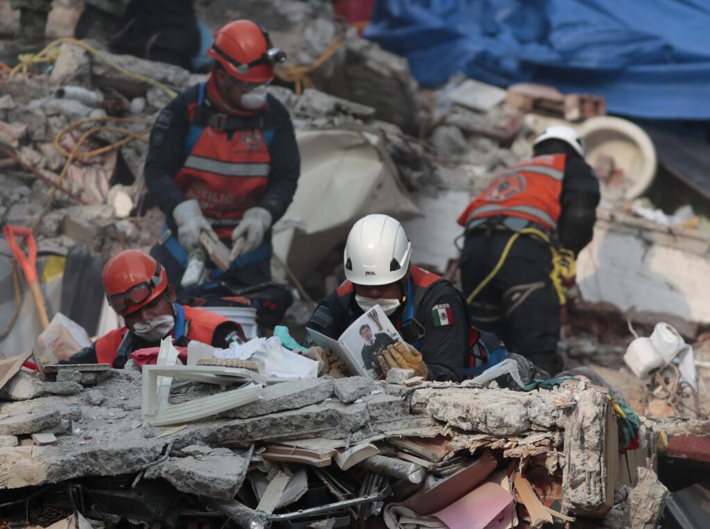 Rescue personnel look through a photo album as they work in rescue operations in the rubble of a building felled by a 7.1 magnitude earthquake, in the Ciudad Jardin neighborhood of Mexico City, Thursday, Sept. 21, 2017. Thousands of professionals and volunteers are working frantically at dozens of wrecked buildings across the capital and nearby states looking for survivors of the powerful quake that hit Tuesday. (AP Photo/Eduardo Verdugo)