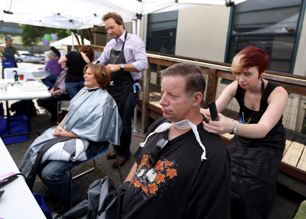 Alivia Alvarez, right, with Calypso Salon, cuts the hair of Robert White while and Greg Stroud also with Calypso Salon, top, cuts the hair of Joyce Kanell during the wellness fair for the homeless in Santa Rosa, Friday, May 22, 2015. (CRISTA JEREMIASON / The Press Democrat)