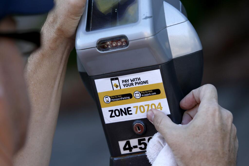 Dale Bohling, a skilled maintenance worker with the city of Santa Rosa, applies stickers to parking meters alerting the public to a new phone app for parking meter payment. Photo taken in Santa Rosa, on Tuesday, Sept. 1, 2015. (BETH SCHLANKER/ The Press Democrat)