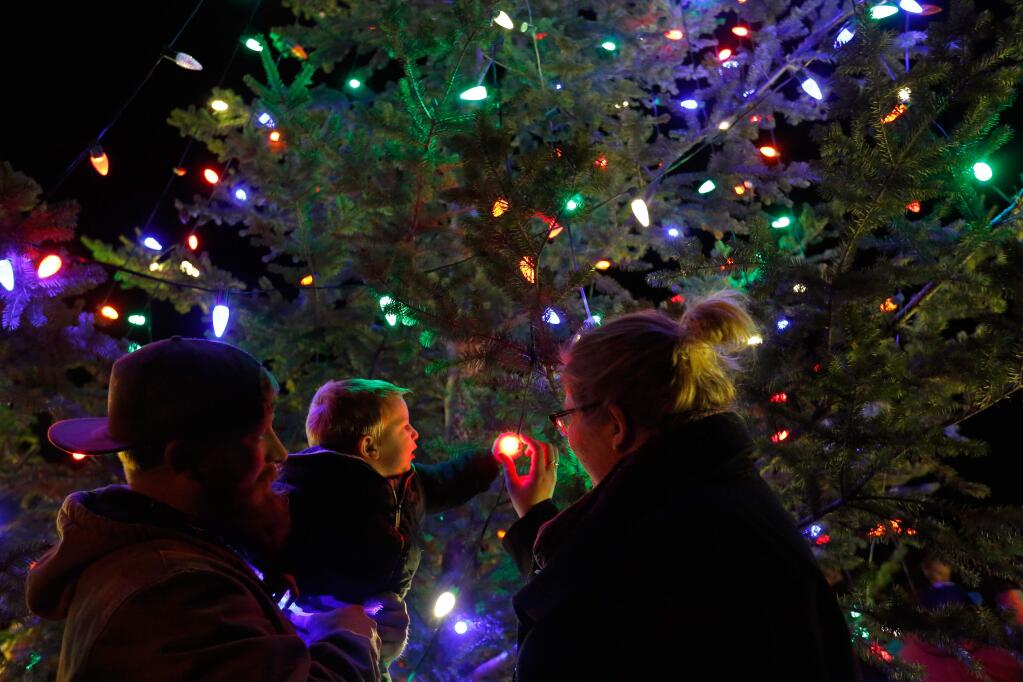 One-year-old Dwight Didier examines the lights on the Geyserville Christmas tree with his father Jacob and aunt Rachel Bailey before the Lighted Tractor Parade in Geyserville, California on Saturday, November 28, 2015. (Alvin Jornada / The Press Democrat)