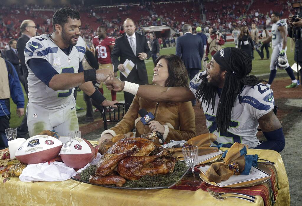 Seattle Seahawks quarterback Russell Wilson, left, celebrates with cornerback Richard Sherman, right, as they sit at a table with sideline reporter Michele Tafoya after the Seahawks beat the San Francisco 49ers 19-3 in an NFL football game in Santa Clara, Calif., Thursday, Nov. 27, 2014. (AP Photo/Marcio Jose Sanchez)