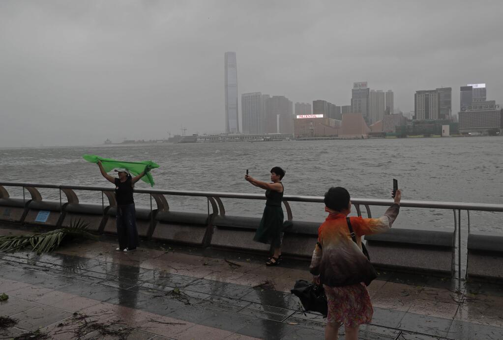 Mainland Chinese tourists take pictures against the wind caused by Typhoon Hato on the waterfront of Victoria Habour in Hong Kong, Wednesday, Aug. 23, 2017. A powerful typhoon barreled into Hong Kong on Wednesday, forcing offices and schools to close and leaving flooded streets, shattered windows and hundreds of canceled flights in its wake. (AP Photo/Vincent Yu)