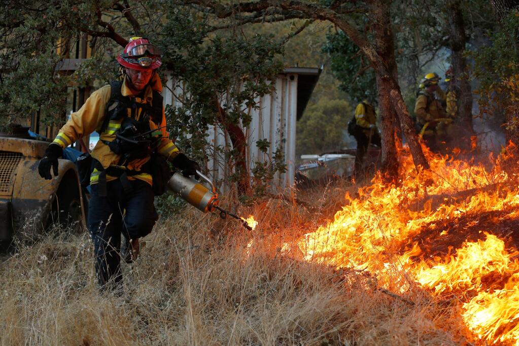 Southern Marin Fire Protection District captain Doug Paterson uses a drip torch to light a backing fire to protect structures in the hills north of Highway 12, in Santa Rosa, California, on Saturday, October 14, 2017. (Alvin Jornada / The Press Democrat)