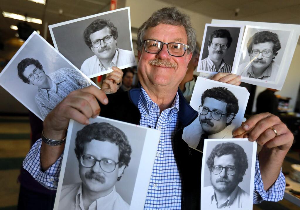 Newsroom colleagues stand behind Chris Smith in the PD newsroom in 2018 and hold some of the photos taken of him throughout his more than 40 years of writing for the paper. (John Burgess/The Press Democrat)