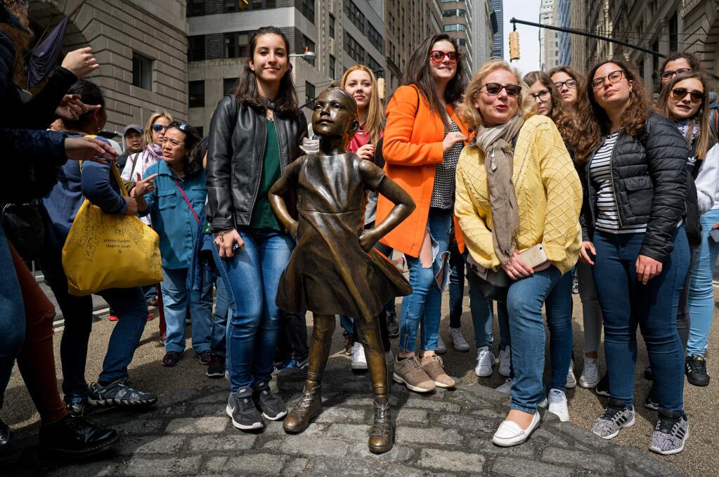 FILE - In this April 12, 2017 file photo, people gather at the 'Fearless Girl' sculpture in lower Manhattan, New York. After she came to prominence staring down a symbol of Wall Street, a bronze bull at the foot of Broadway, New York City's Fearless Girl statue will be moving to a new home next to the New York Stock Exchange later in 2018. (AP Photo/Craig Ruttle, File)