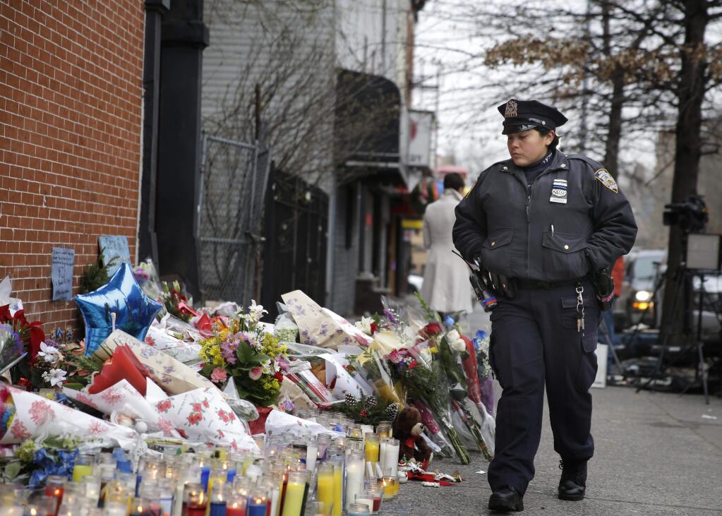 A New York City police officer looks over a makeshift memorial near the site where fellow officers Rafael Ramos and Wenjian Liu were murdered in the Brooklyn borough of New York, Monday, Dec. 22, 2014. Police say Ismaaiyl Brinsley ambushed the two officers in their patrol car in broad daylight Saturday, fatally shooting them before killing himself inside a subway station. (AP Photo/Seth Wenig)