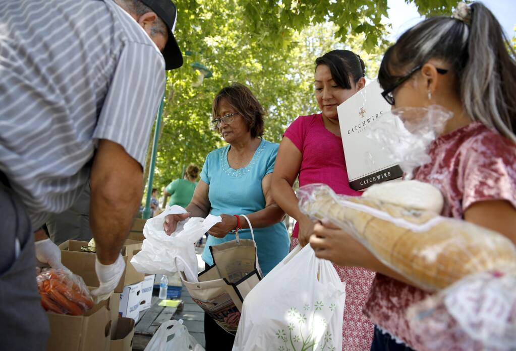 (From right) Anahi Hernandez, 8, her mother Maria Camacho, and grandmother Magda Huerta fill their bags with food donated through the Redwood Empire Food Bank's Station 3990 program at Martin Luther King Jr. Park in Sonoma on Thursday, July 12, 2018. (Beth Schlanker/ The Press Democrat)