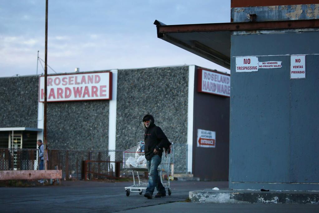 Pedro Garcia makes his way past two unoccupied buildings along Sebastopol Road in the unincorporated area of Roseland on Tuesday. (Conner Jay/The Press Democrat)