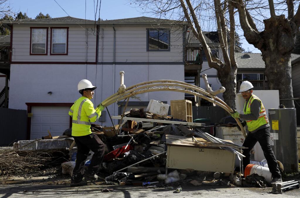 Antonio Zuniga, left, and Geraldo Lemus, employees with Pacific Sanitation work to dispose of water damaged belongings and debris along the sidewalk in Guerneville on Monday, March 11, 2019. (BETH SCHLANKER/ The Press Democrat)