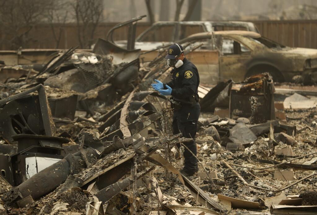 FILE - In this Thursday, Nov. 15, 2018 file photo, a Sheriff's deputy looks for human remains at a home burned in the Camp fire in Magalia, Calif. Searchers are in a race against time with long-awaited rains expected in the Northern California fire zone where dozens of bodies have been recovered so far. While the rain is good for tamping down the still-burning fire, it will turn the fire zone into a muddy mess and make it more difficult for crews to search. (AP Photo/John Locher, File)