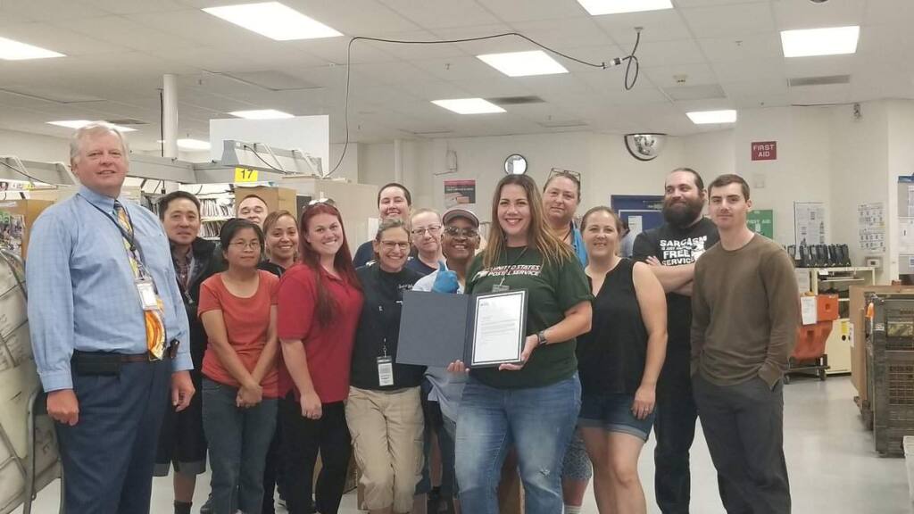 Postal worker Chey Kahaulelio-Virelas, shown with her Windsor co-workers, is honored with a letter from the U.S. Postmaster General Megan J. Brennan on Tuesday, July 9, 2019. (U.S. POSTAL SERVICE)