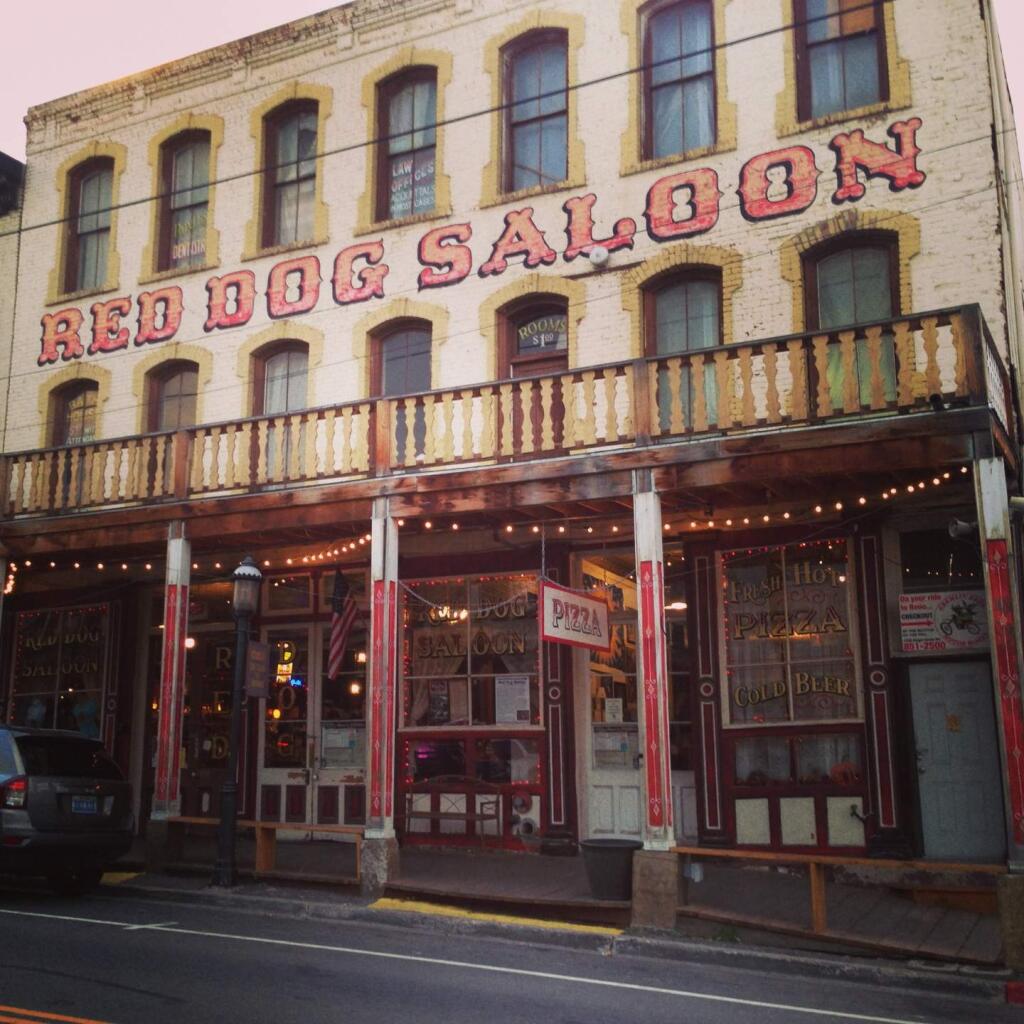 Enjoy a pizza and live music at the iconic Red Dog Saloon. Below, a sign welcomes visitors to the city.