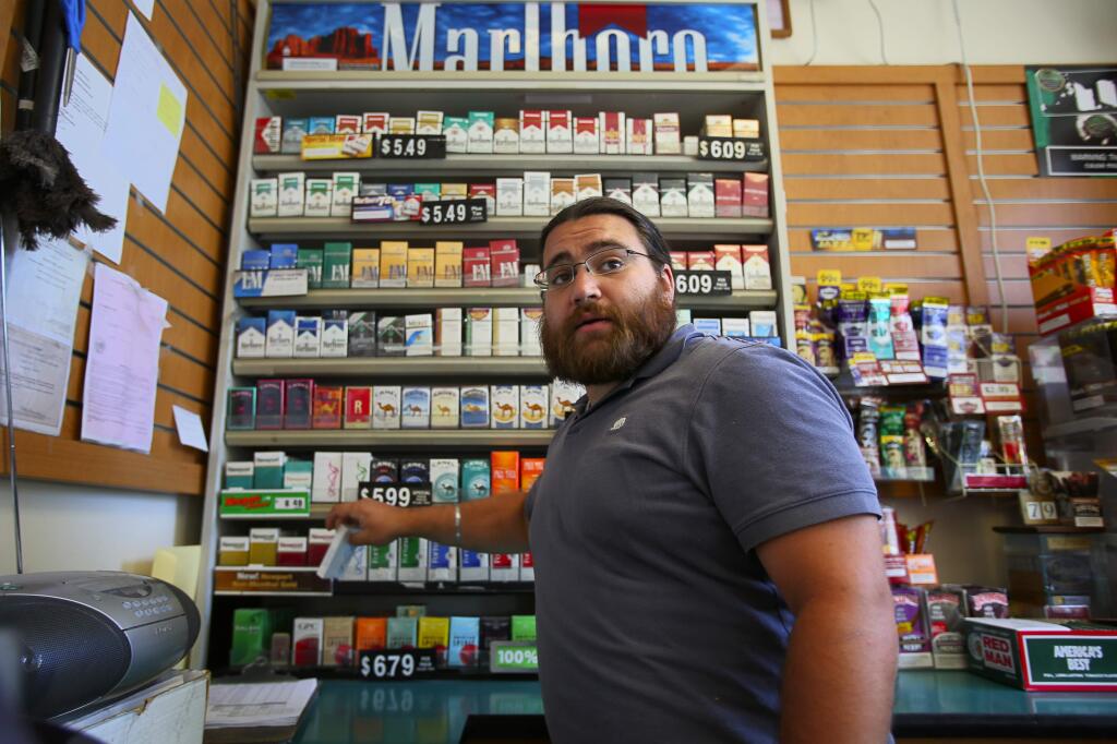 Aman Gill grabs a pack of cigarettes for a customer at his family's Fast Lane gas station, in Healdsburg, on Tuesday, June 30, 2015. (Christopher Chung / The Press Democrat)