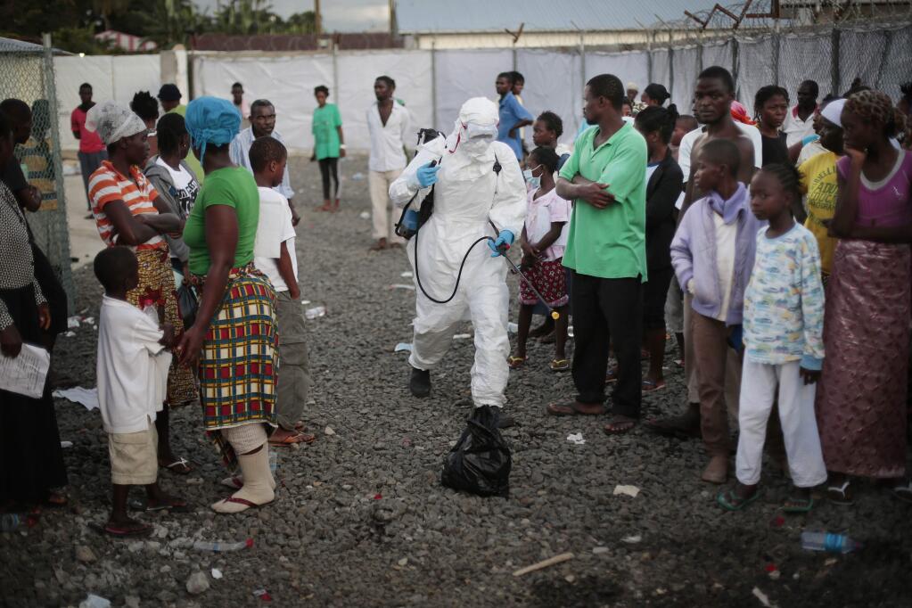In this Tuesday, Sept. 30, 2014, file photo a medical worker sprays people being discharged from the Island Clinic Ebola treatment center in Monrovia, Liberia. (AP Photo/Jerome Delay, File)