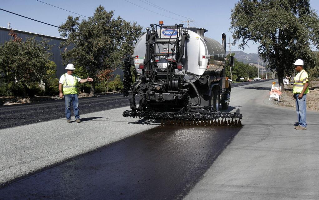A road crew applies a sealer to Eighth Street East in a previous year's work. Crews will apply overlays, new pavement and sealers to a number of roads and bridges across Sonoma County as part of a multi-year project to improve county roads. (The Press Democrat / Jeff Kan Lee)