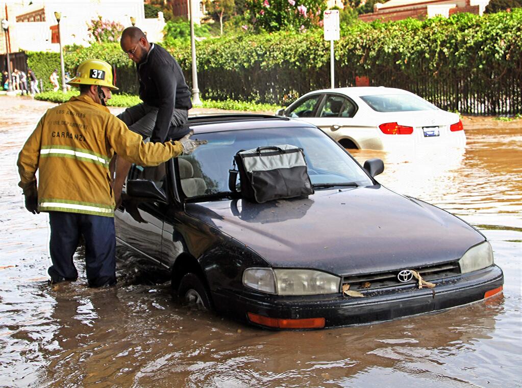 A Los Angeles firefighter helps a driver whose car became stranded on Sunset Boulevard after a 30-inch water main broke and sent water flooding down Sunset and onto the UCLA campus in the Westwood section of Los Angeles Tuesday, July 29, 2014. (AP Photo/Steve Gentry)