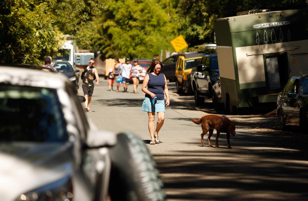 Local resident Dawne Gilmore walks her dog Quincy between rows of parked cars along River Drive near the entrance to Mother's Beach in Forestville, California, on Saturday, June 30, 2018. (Alvin Jornada / The Press Democrat)