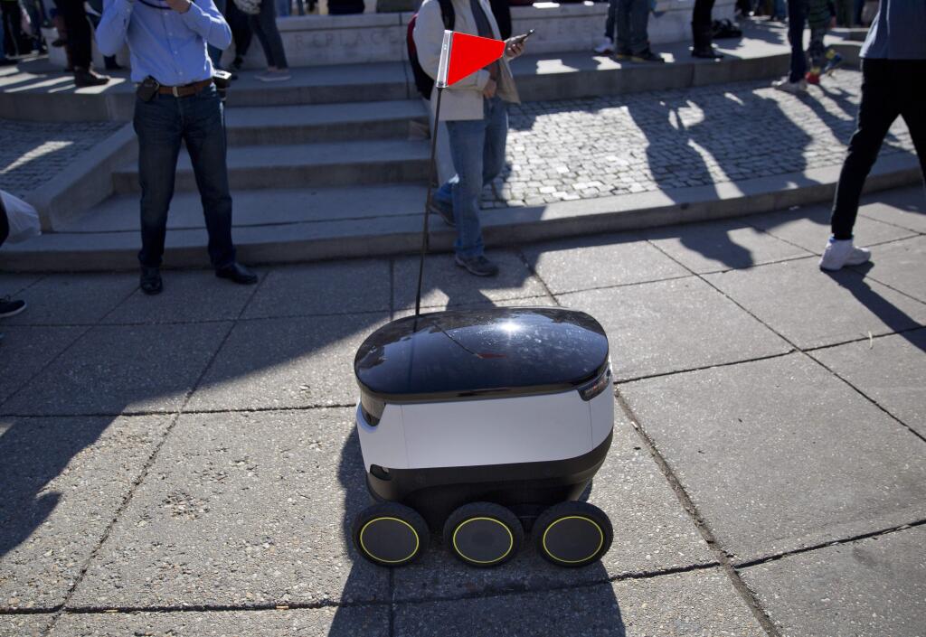 FILE - In this Feb. 20, 2017, file photo, a six-wheeled ground delivery robot, from Starship Technologies, shares the sidewalk with pedestrians at DuPont Circle in Washington, D.C. Delivery robots in San Francisco will need permits before they can roam city sidewalks under legislation approved by supervisors on Tuesday, Dec. 5, 2017. (AP Photo/Pablo Martinez Monsivais, file)