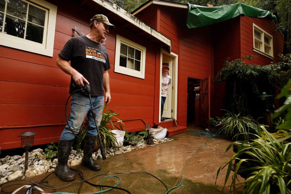 Brian Bennett chats with his wife Laura while power washing mud left by receded flood water at their home beside Austin Creek in Cazadero, California, on Saturday, March 2, 2019. (Alvin Jornada / The Press Democrat)