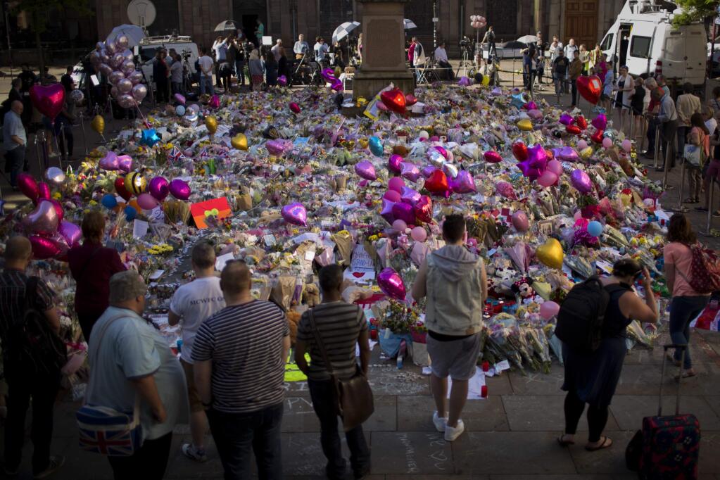 People stand next to flowers for the victims of Monday's bombing at St Ann's Square in central Manchester, England, Friday, May 26 2017. British police investigating the Manchester Arena bombing arrested a ninth man while continuing to search addresses associated with the bomber. (AP Photo/Emilio Morenatti)