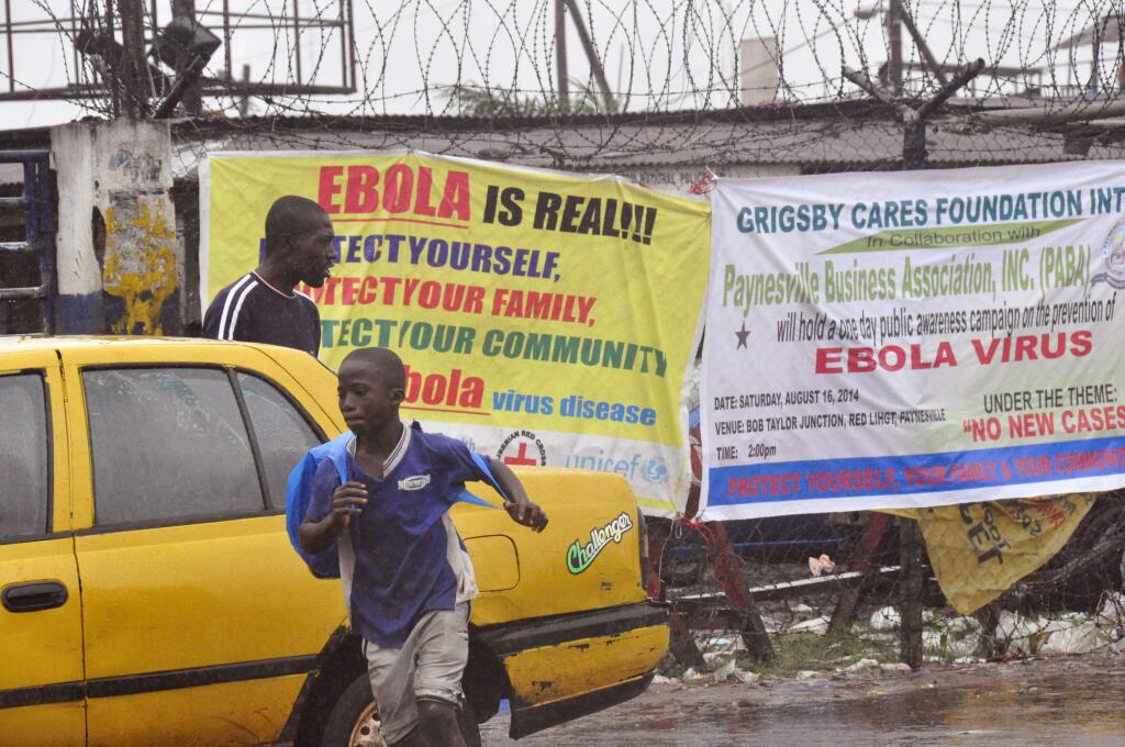 People pass by Ebola virus health warning signs, in the city of Monrovia, Liberia, Sunday, Aug. 17, 2014. Liberian officials fear Ebola could soon spread through the capital's largest slum after residents raided a quarantine center for suspected patients and took items including blood-stained sheets and mattresses. (AP Photo/Abbas Dulleh)