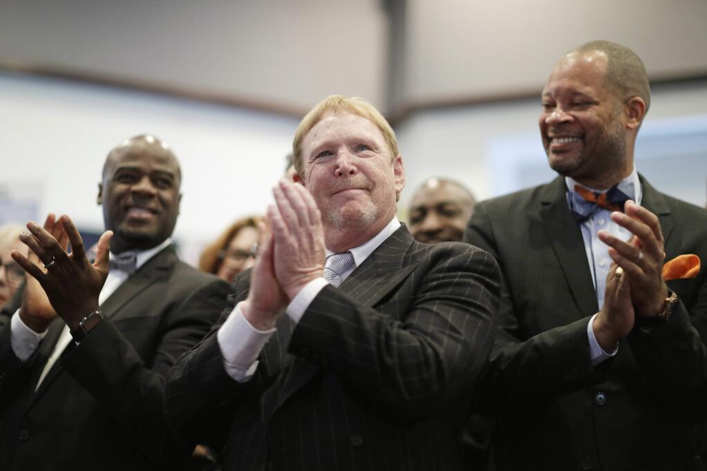 FILE - In this Monday, Oct. 17, 2016, file photo, Oakland Raiders owner Mark Davis, center, claps as he attends a bill signing ceremony with Nevada Gov. Brian Sandoval in Las Vegas. Sandoval signed a bill into law that clears the way for a Las Vegas stadium that could be home to both UNLV football and the Raiders. Several owners insisted it's far too early to reach any conclusions in the Raiders' relocation issue. But Commissioner Roger Goodell supported Davis' assertion there has been no movement toward keeping the franchise in the Bay Area, (AP Photo/John Locher, File)