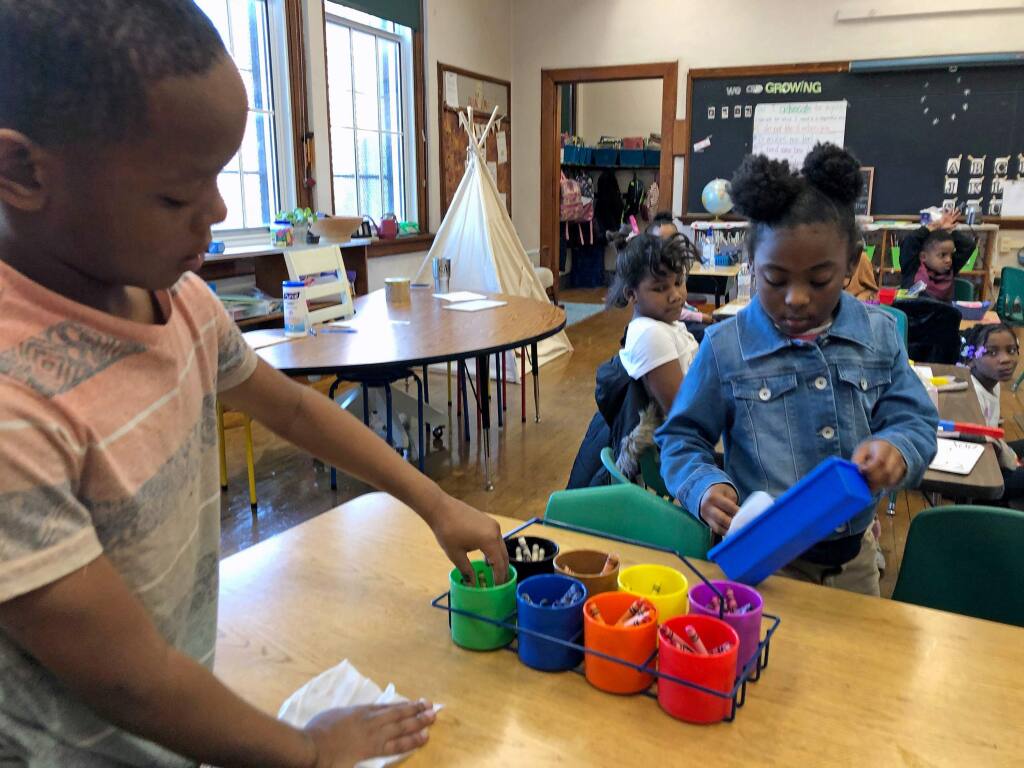 First graders Anthony Chatman, left, and Malaysia Freeman wipe down a play table and items on it with hand wipes at Patrick Henry Elementary School in St. Louis on Tuesday, March 3, 2020. The school district, amid Coronavirus concerns, last week purchased hand wipes and sanitary soap for every classroom. (AP Photo/Jim Salter)