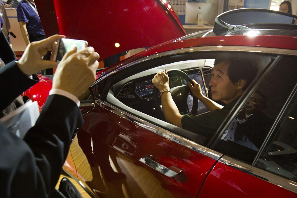 FILE - In this Monday, April 25, 2016, file photo, a visitor poses for a smartphone photo while sitting in the driver's seat of a Tesla Model S electric car on display at the Beijing International Automotive Exhibition in Beijing. (AP Photo/Mark Schiefelbein, File)
