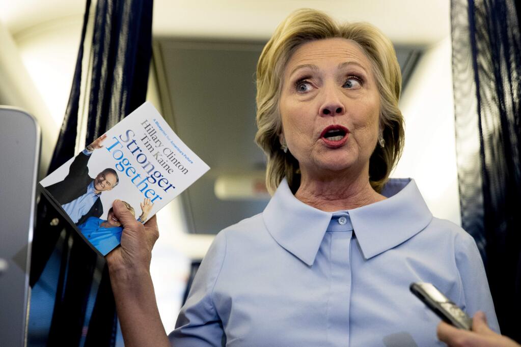 Democratic presidential candidate Hillary Clinton holds up a book entitled 'Stronger Together' as she speaks to members of the media on her campaign plane while traveling to Quad Cities International Airport in Moline, Ill., Monday, Sept. 5, 2016. (AP Photo/Andrew Harnik)