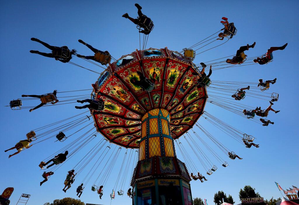 Riders fly through the air above the midway on the Wave Swinger ride at the opening day of the Sonoma County Fair. (photo by John Burgess/The Press Democrat)