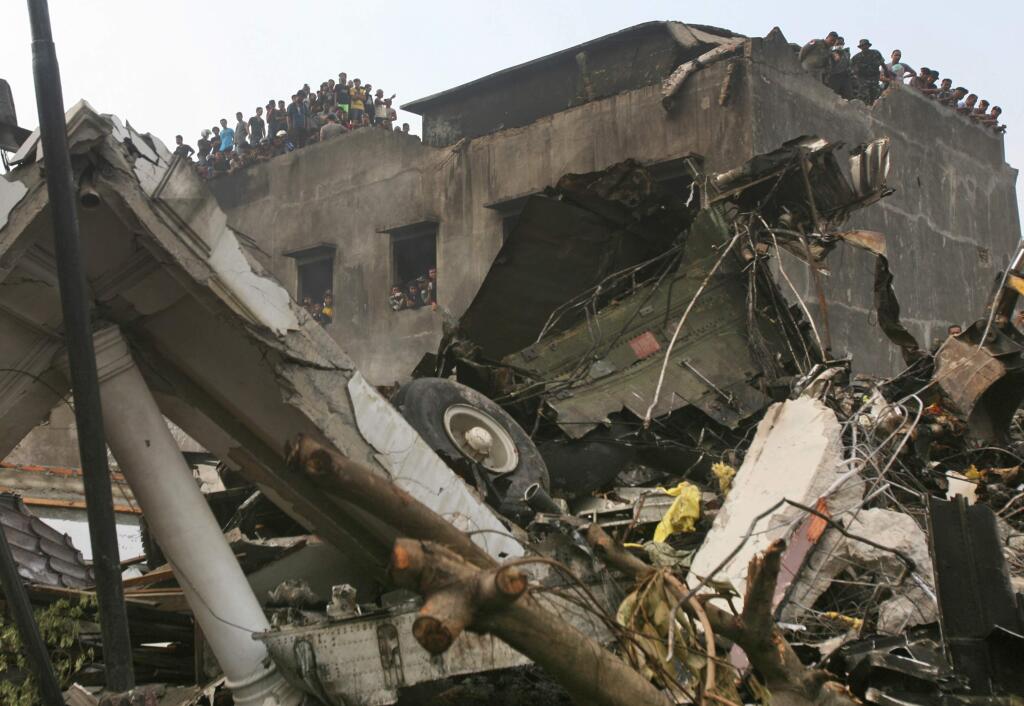 Residents examine the wreckage of an Indonesian Air Force cargo plane from a building next to the site where it crashed in Medan, North Sumatra, Indonesia, Tuesday, June 30, 2015. The C-130 Hercules plane has crashed into a residential neighborhood in the country's third-largest city. (AP Photo/Binsar Bakkara)