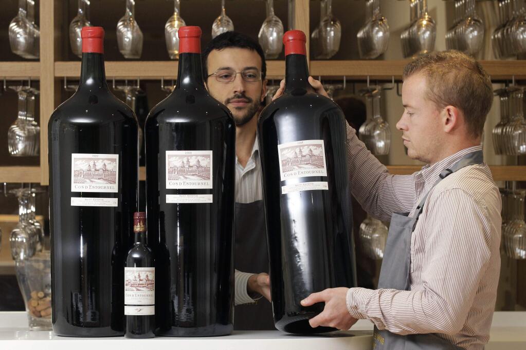 FILE - This is a Thursday, Nov. 17, 2011 file photo of Antique Wine Company's employees poses with three Melchiors and a standard size bottle of Cos D'Estournel wine at the wine merchant in London, Thursday, Nov. 17, 2011. A Melchior holds 18 litres, 24 bottles or 102 glasses of wine. The free online dictionary of current usage, created by the publishers of the venerable Oxford English Dictionary, issued its quarterly update Thursday Aug. 27, 2015 of new words that have gained widespread currency in the English language. From the list comes, 'wine o'clock' the appropriate time of day to start drinking wine. (AP Photo/Sang Tan, File)