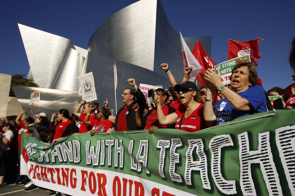 FILE - In this Dec. 15, 2018, file photo, United Teachers Los Angeles leaders are joined by thousands of teachers march past the Walt Disney Concert Hall in Los Angeles. Strike or no strike, after a deal is ultimately reached on a contract for Los Angeles teachers, the school district will still be on a collision course with deficit spending because of pensions and other financial obligations. School systems across California are experiencing burdensome payments to the state pension fund while struggling to improve schools. (AP Photo/Damian Dovarganes, File)