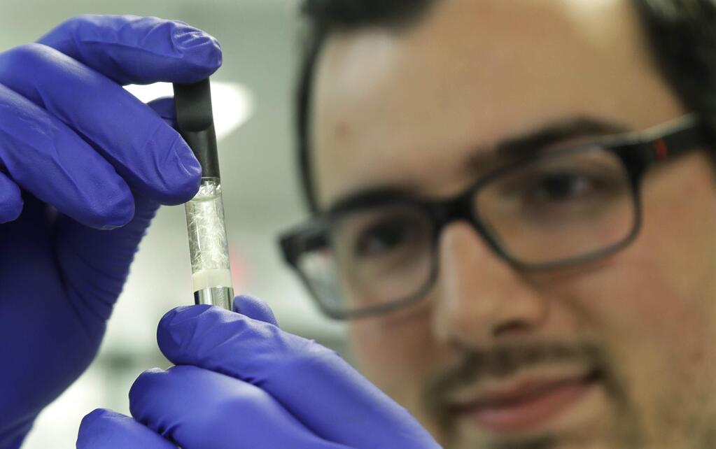 Pierce Prozy examines a Yolo! brand CBD vape oil cartridge at Flora Research Laboratories in Grants Pass, Ore., on July 19, 2019. The Associated Press commissioned the lab to test vape products marketed as delivering the cannabis extract CBD. AP chose samples by targeting brands that law enforcement authorities or users flagged as suspect. Ten of the 30 samples contained synthetic marijuana, a dangerous street drug commonly known as K2 or spice. (AP Photo/Ted Warren)