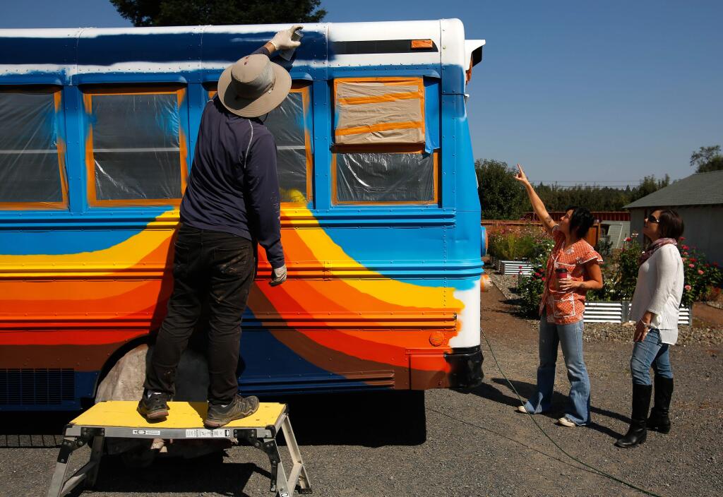 Muralist Ricky Watts, left, paints the schoolbus exterior while Schoolbox Project founder Belle Sweeney and child protection officer Monica Julian , right, discuss details during the retrofitting of the schoolbus by members of the Schoolbox Project in Sebastopol, California, on Sunday, September 17, 2017. The schoolbus is being transformed into a mobile classroom that will be brought to areas of Houston, Texas affected by Hurricane Harvey. (Alvin Jornada / The Press Democrat)