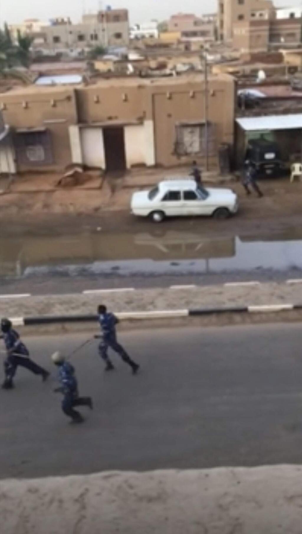 In this image made from video, Police officers running down a street in Khartoum, Sudan, on Monday, June 3, 2019. Sudanese security forces moved against a protest sit-in camp in the capital Monday, witnesses and protest organizers said. Machine gun fire and explosions were heard and smoke rose from the area. Protest organizers said at least two people were killed. (Elmontasir Darwish via AP)