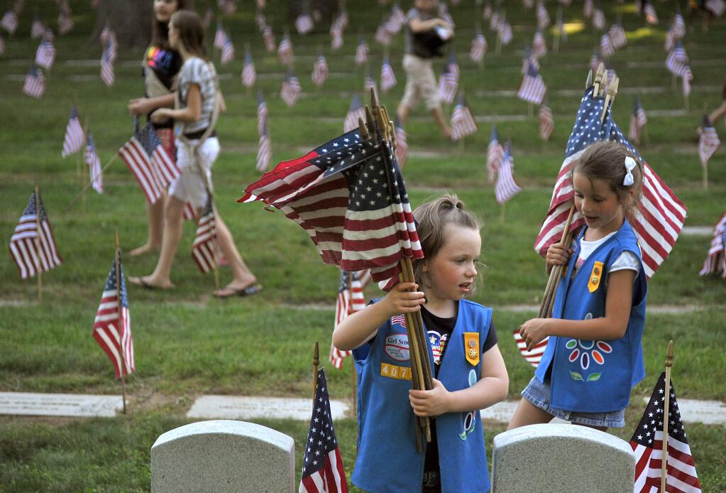 FILE - In this May 23, 2012 file photo, Natalie Benson, 5, and Holly Sweezer, 6, carry extra flags as Boy and Girl Scouts place flags on each of the 5,000 headstones at the Grand Rapids Veterans State Cemetery in Grand Rapids, Mich. The Wednesday, Oct. 11, 2017 Boy Scouts of America announcement to admit girls throughout its ranks will transform what has been a mostly cordial relationship between the two iconic youth groups since the Girl Scouts of the USA was founded in 1912, two years after the Boy Scouts. (Katie Greene/The Grand Rapids Press via AP)