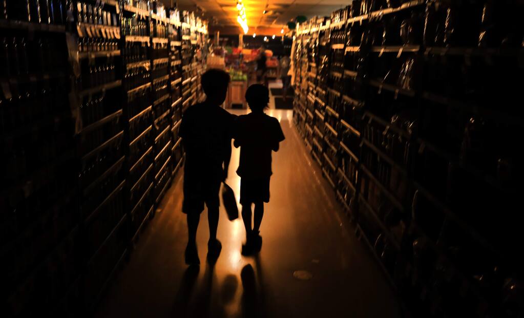 Elijah Carter, 11, left, and Robert Haralson, 12, help shop for their parents in a darkened Oliver’s Supermarket in Rincon Valley, Wednesday, Oct. 23, 2019. The west side of the store was lit by patio lights powered by a generator as power was shut off again by PG&E due to fire danger. (Kent Porter / The Press Democrat)