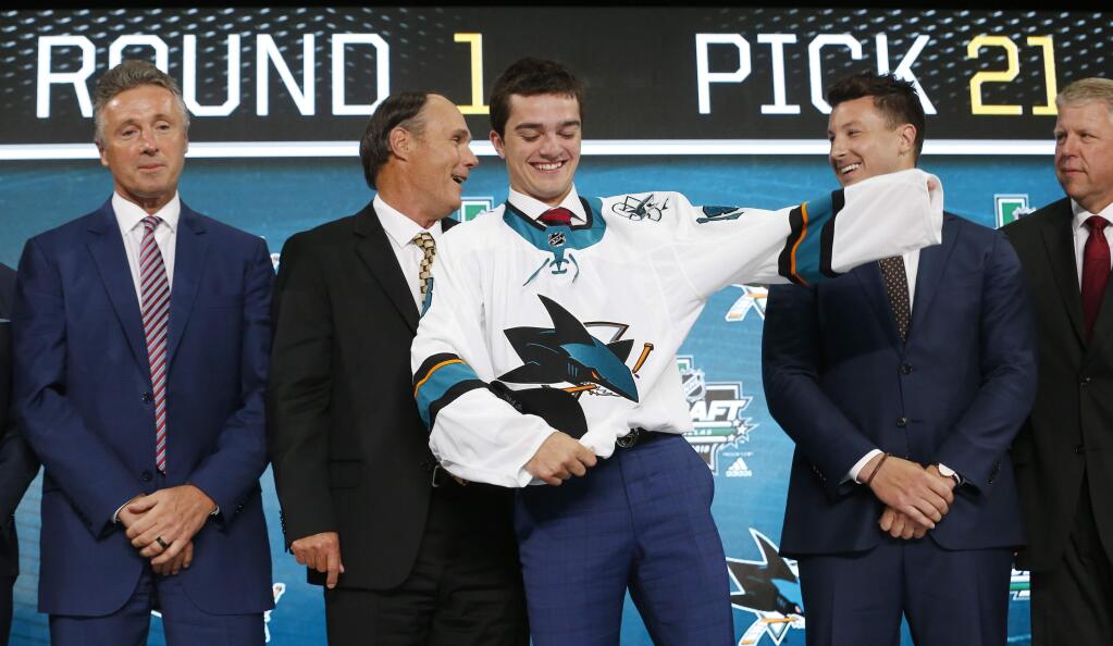 Ryan Merkley, center, of Canada, puts on a jersey after being selected by the San Jose Sharks during the NHL hockey draft in Dallas, Friday, June 22, 2018. (AP Photo/Michael Ainsworth)